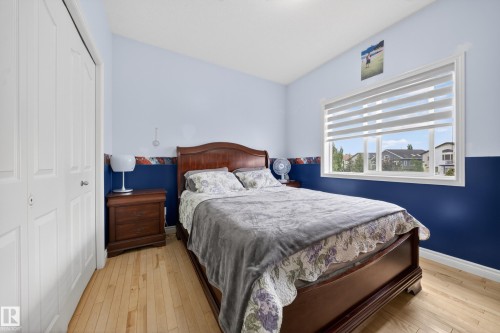 Bright bedroom featuring light wood-finish flooring, a large window with horizontal blinds, and a double bi-fold closet - 4113 59 Street, Beaumont, AB 