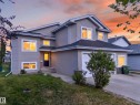 Two-story residence featuring light gray siding, an attached garage, a dark entry door with decorative glass, white-trimmed windows, and a concrete driveway - 4113 59 Street, Beaumont, AB 