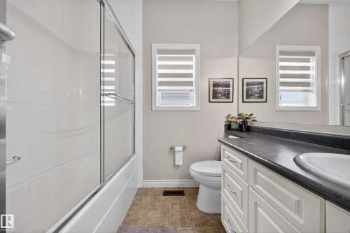 Bathroom featuring a white bathtub with sliding glass doors, white subway tile surround, a white vanity with paneled cabinetry, dark countertop, and an integrated sink - 4113 59 Street, Beaumont, AB 