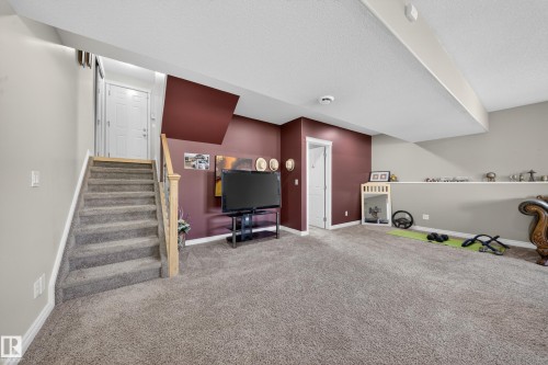Carpeted lower level featuring a staircase with light wood newel posts, a white paneled door, and a built-in shelf along one wall - 4113 59 Street, Beaumont, AB 