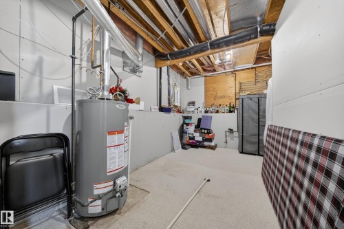 Utility room with exposed ceiling joists and ductwork, featuring a water heater, carpeted flooring, and partially finished walls - 4113 59 Street, Beaumont, AB 