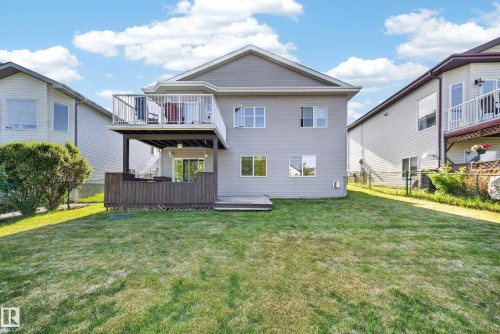 Expansive backyard with a manicured lawn, featuring a two-story exterior with a second-level deck, a covered patio, and a ground-level deck - 4113 59 Street, Beaumont, AB 