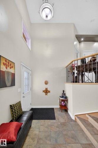 Foyer featuring multi-toned tile flooring, a white paneled entry door with decorative glass inserts, and a high ceiling with a mounted light fixture - 4113 59 Street, Beaumont, AB 