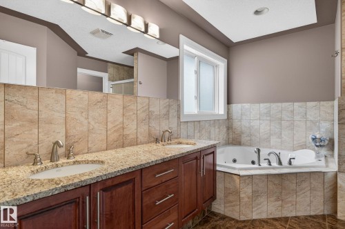 Kitchen featuring rich wood cabinetry, stainless steel appliances, a center island with integrated wine storage, granite-style countertops, and tile flooring - 1508 Palmer Close, Edmonton, AB 