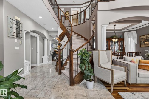 Brick exterior with stacked stone accents, arched double entry doors, a white garage door, concrete stairs, and a mature evergreen shrub - 1508 Palmer Close, Edmonton, AB 