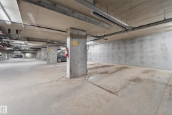 Concrete subterranean parking area featuring exposed ceiling utilities and structural columns - 