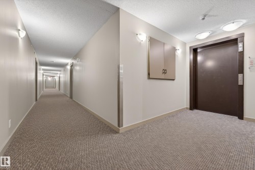 Elevator lobby featuring a dark wood-finish door with brushed metal controls, overhead flush-mount lighting, and sconce lighting - 225 1510 Watt Drive, Edmonton, AB - Indoor Photo Showing Other Room