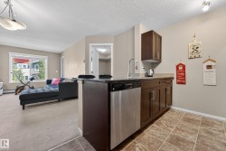 Contemporary kitchen area featuring wood-finish cabinetry, stainless steel dishwasher, and a dark stone countertop - 