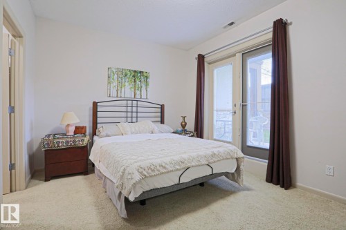 Carpeted bedroom featuring a light-colored headboard, neutral wall paint, and a hinged glass door with a screen - 117 160 Magrath Road, Edmonton, AB - Indoor Photo Showing Bedroom