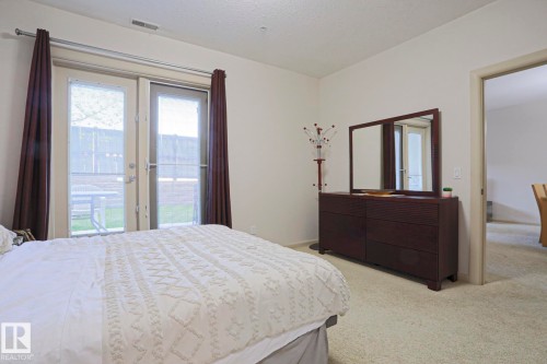 Carpeted room with double glass-paneled doors opening to an exterior patio - 117 160 Magrath Road, Edmonton, AB - Indoor Photo Showing Bedroom