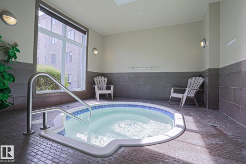 Indoor hot tub with a stainless steel grab rail, mosaic tile detailing, and a large window - 117 160 Magrath Road, Edmonton, AB - Indoor Photo Showing Other Room