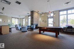 Spacious common room featuring textured carpeting, a stone-clad fireplace, and multiple large windows - 
