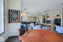 Spacious communal area featuring a built-in kitchen with wood cabinetry and a breakfast bar, a stone accent wall with a fireplace, track lighting, and carpeted flooring - 