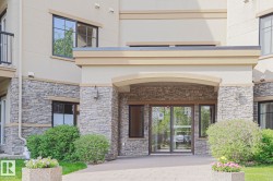 Building entrance featuring stacked stone facade, automatic glass doors, arched portico, perimeter landscaping, and paver walkway - 