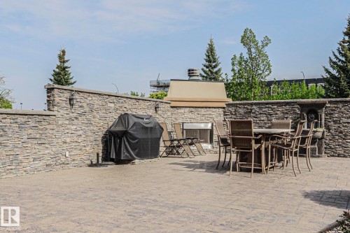 Expansive outdoor patio featuring stamped concrete flooring, stone veneer walls, a built-in outdoor fireplace, and integrated wall sconces - 117 160 Magrath Road, Edmonton, AB - Outdoor