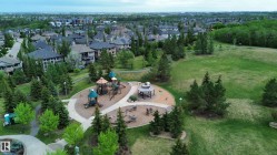 Expansive parkland featuring a playground structure with multiple slides and climbing elements, a covered gazebo, and paved walking paths - 