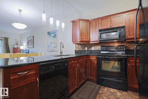 Kitchen featuring dark wood cabinetry, black appliances, a black countertop, a tile backsplash, and recessed lighting - 117 160 Magrath Road, Edmonton, AB - Indoor Photo Showing Kitchen