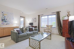 Living area featuring light-colored carpeting, a large window with blinds and drapes, and a glass-top coffee table with a geometric base - 