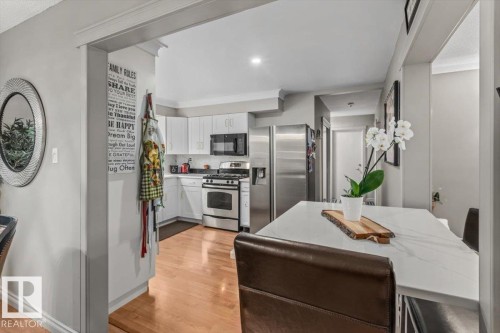 Open-concept kitchen featuring white cabinetry, stainless steel appliances, and wood-finish flooring - 6720 29 Avenue, Edmonton, AB 