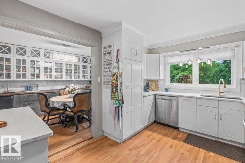 Bright kitchen featuring white cabinetry, stainless steel appliances, a window over the sink, wood-finish flooring, and a quartz countertop - 6720 29 Avenue, Edmonton, AB 