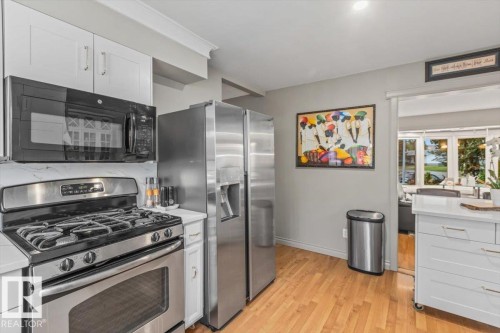 Kitchen featuring stainless steel appliances, white cabinetry, wood-finish flooring, and light-toned countertops - 6720 29 Avenue, Edmonton, AB 