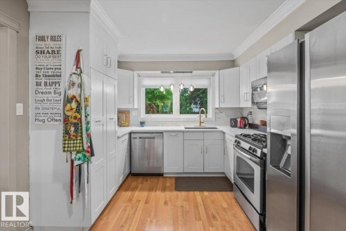 Contemporary kitchen featuring white cabinetry, stainless steel appliances, wood-finish flooring, white countertops, and a window above the sink - 6720 29 Avenue, Edmonton, AB 