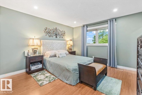 Primary Bedroom featuring wood-finish flooring, light green walls, and a large window with privacy blinds - 6720 29 Avenue, Edmonton, AB 