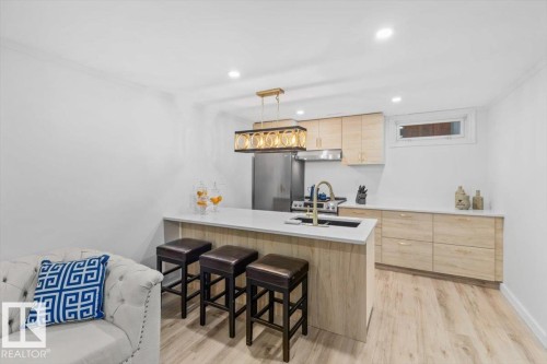 Modern kitchen featuring a light wood-finish island with a white countertop and gold-tone faucet - 6720 29 Avenue, Edmonton, AB 