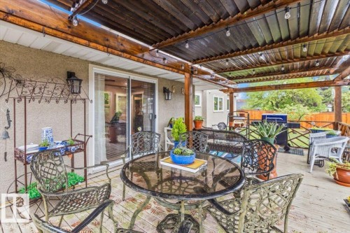 Expansive outdoor deck featuring a wood pergola with string lighting, a concrete-textured exterior wall, and a sliding glass door - 6720 29 Avenue, Edmonton, AB 