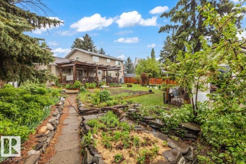 Expansive backyard featuring a stone pathway, multiple garden beds with rock borders, and mature perimeter trees - 6720 29 Avenue, Edmonton, AB 
