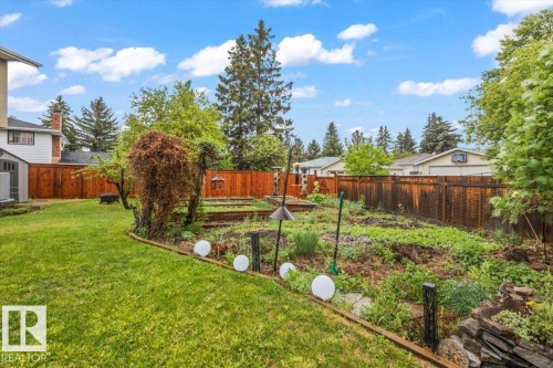 Expansive backyard featuring a manicured lawn, established garden beds, mature trees, and a privacy fence - 6720 29 Avenue, Edmonton, AB 