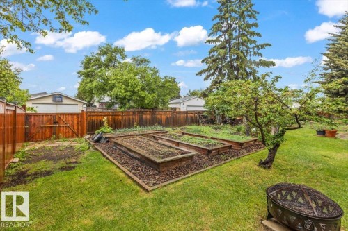 Expansive backyard featuring a manicured lawn, multiple raised garden beds, mature trees, a wooden privacy fence, and a decorative fire pit - 6720 29 Avenue, Edmonton, AB 