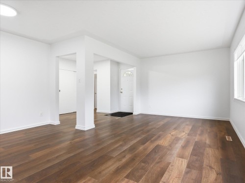 Spacious interior featuring wood-finish flooring, white walls, and a front entry door with decorative glass - 13316 136 Avenue, Edmonton, AB 