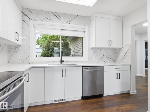 Modern kitchen featuring white cabinetry, integrated stainless steel appliances, a black matte pull-down faucet, and a large window above the sink - 13316 136 Avenue, Edmonton, AB 