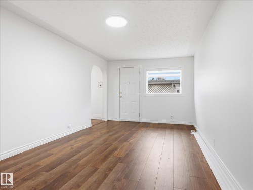 Spacious room featuring wood-finish flooring, white walls, and a round flush-mount ceiling light - 13316 136 Avenue, Edmonton, AB 