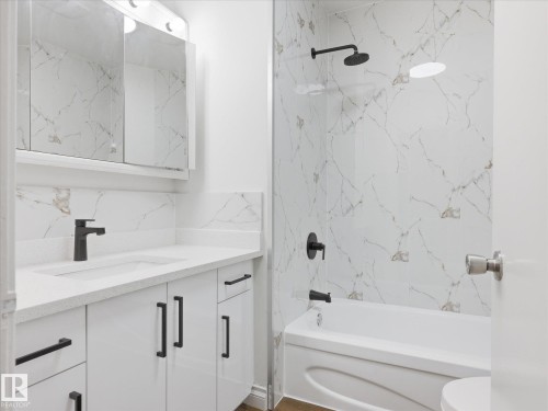 Contemporary bathroom featuring a white vanity with black hardware, an integrated sink with a matte black faucet, and a wall-mounted mirrored cabinet - 13316 136 Avenue, Edmonton, AB 
