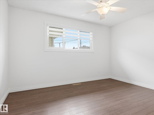 Bright room featuring wood-finish flooring, white walls, and a multi-pane window with horizontal blinds - 13316 136 Avenue, Edmonton, AB 