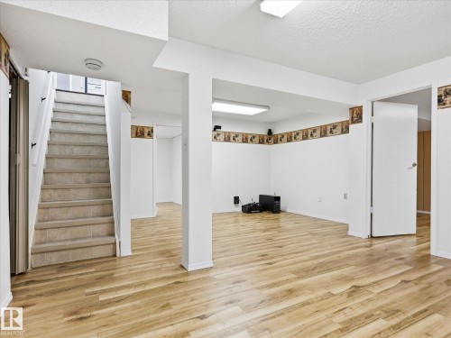 Open-concept room featuring wood-finish flooring, white walls, and a recessed staircase with tiled steps - 13316 136 Avenue, Edmonton, AB 