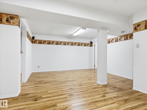 Spacious interior room featuring wood-finish flooring, white walls with decorative border, recessed ceiling lighting, and exposed structural pillars - 13316 136 Avenue, Edmonton, AB 