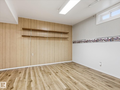 Room featuring wood-finish flooring, two walls with wood paneling, and two walls with white paint below a patterned wallpaper border - 13316 136 Avenue, Edmonton, AB 