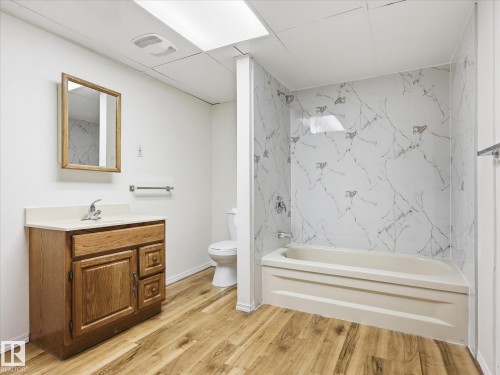 Bathroom featuring wood-finish flooring, a wood-framed mirror, a vanity with a white countertop, and a shower/tub combination with a white and gray marbled surround - 13316 136 Avenue, Edmonton, AB 