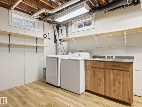 Utility space featuring wood-finish flooring, a utility sink with wood cabinetry, and a washer and dryer - 13316 136 Avenue, Edmonton, AB 