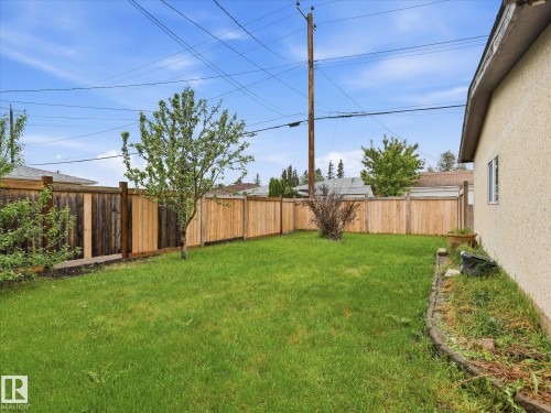 Fenced backyard featuring a large grass area, mature trees, and a stucco exterior - 13316 136 Avenue, Edmonton, AB 