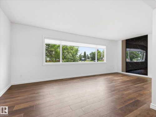 Bright interior space featuring wood-finish flooring, white walls, and a large multi-pane window - 13316 136 Avenue, Edmonton, AB 