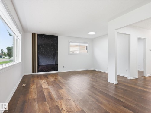 Open-concept interior featuring wood-finish flooring, a decorative accent wall with dark stone-look paneling and vertical wood slats, and a circular ceiling light fixture - 13316 136 Avenue, Edmonton, AB 