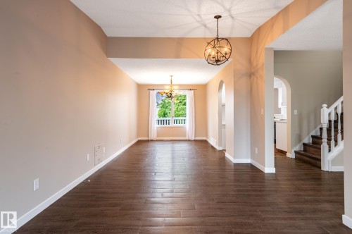 Expansive room featuring wood-finish flooring, a large window with white trim, and two spherical pendant light fixtures - 16811 91 Street, Edmonton, AB 