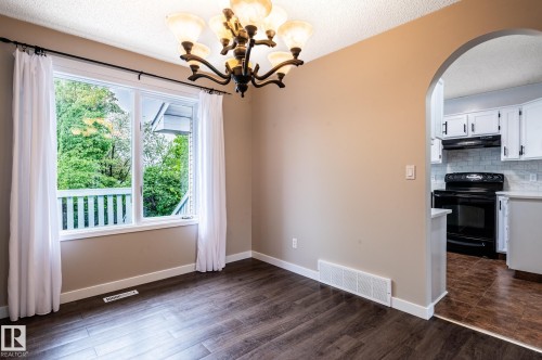 Spacious room featuring wood-finish flooring and a central chandelier - 16811 91 Street, Edmonton, AB 