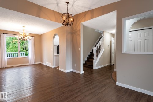 Spacious interior with wood-finish flooring, a contemporary chandelier, and arched doorway - 16811 91 Street, Edmonton, AB 