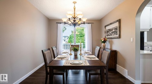 Formal dining area featuring a dark wood-finish table with seating for six, dark wood-finish flooring, a multi-bulb chandelier, and a sliding glass door providing exterior access - 16811 91 Street, Edmonton, AB 