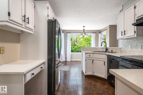 Kitchen featuring white cabinetry with matte black hardware, white subway tile backsplash, black appliances, and a built-in desk area with a light-toned countertop - 16811 91 Street, Edmonton, AB 